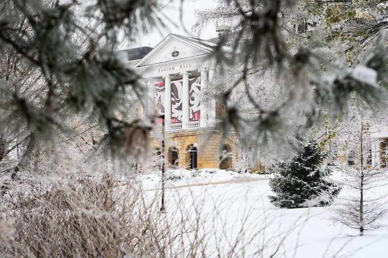 Rime ice coats the branches of trees flanking Bascom Hall on snow-covered Bascom Hill at the University of Wisconsin-Madison during a foggy winter day on Jan. 6, 2021. In between the building’s columns hangs a three panel graphic of UW-Madison mascot Bucky Badger. Unlike hoarfrost – which typical forms on clear, cold nights – rime ice forms when moisture in the foggy air coats nearby surfaces and freezes. (Photo by Jeff Miller / UW-Madison)
